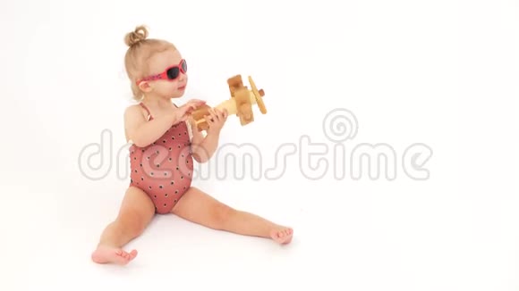 穿着泳衣和太阳镜的金发女婴玩普通木制玩具飞机视频的预览图
