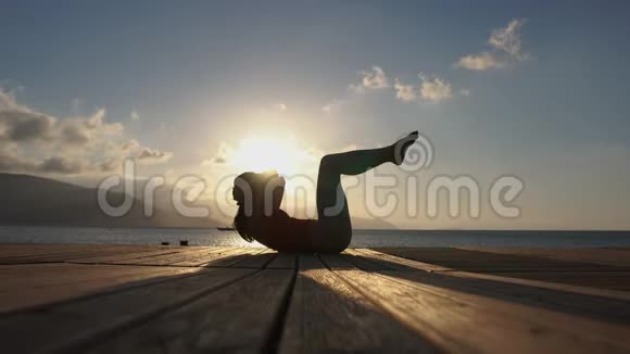 4K一个漂亮的女孩在日出时在海边做腹肌练习动作缓慢视频的预览图