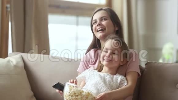 妈妈拿着遥控器和小女儿一起看电视视频的预览图