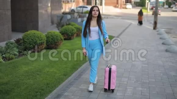 时髦的女商人卷着一个手提箱沿着人行道走视频的预览图