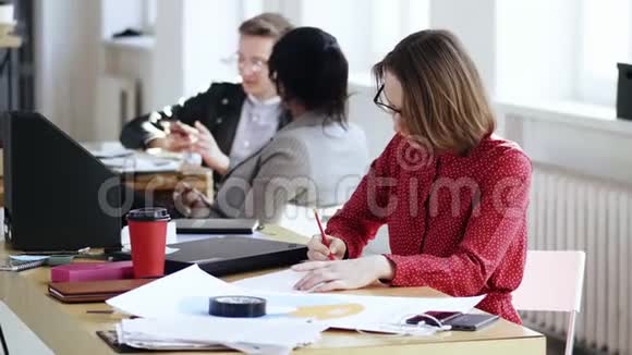 快乐专注的商务女性穿着红色连衣裙忙于文书工作在现代办公桌上写文件视频的预览图