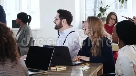 幸福微笑的多民族办公室经理坐在餐桌前嘲笑现代健康工作场所的企业培训研讨会视频的预览图