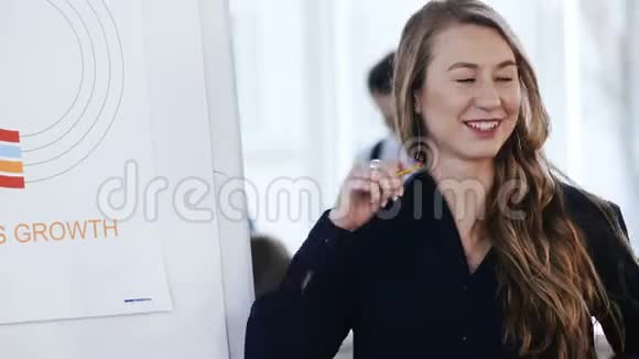 在现代办公会议上一位年轻面带微笑金发碧眼的老板商务女性在销售图表附近与同事交谈视频的预览图