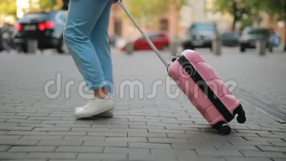一个面目全非的旅游妇女卷着一个手提箱沿着城市的人行道走视频的预览图