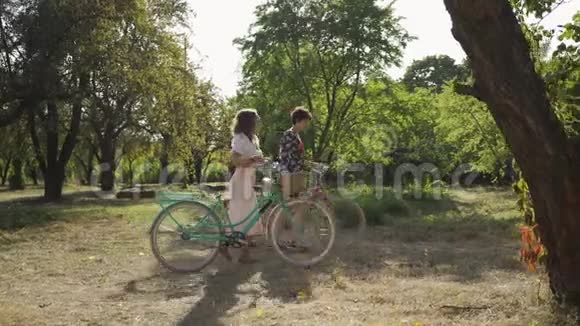 两个可爱的白种人年轻女人在户外散步女孩们一边说话一边骑着自行车走在狭窄的路上视频的预览图