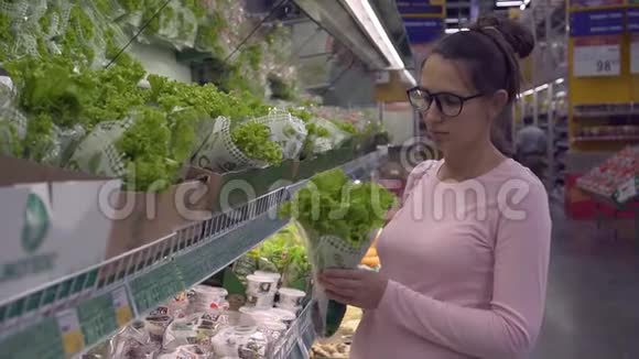 在超市里戴眼镜的年轻孕妇选择新鲜的有机蔬菜女人选择蔬菜视频的预览图