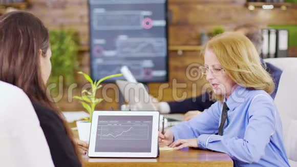 女同事分析会议室平板电脑上的图表视频的预览图