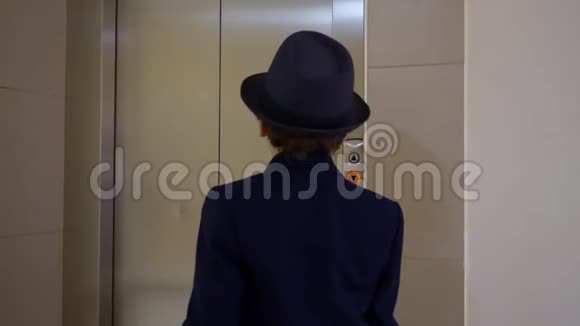 穿着商务服帽子和公文包的小男孩走进电梯后景商人按按钮打电话视频的预览图