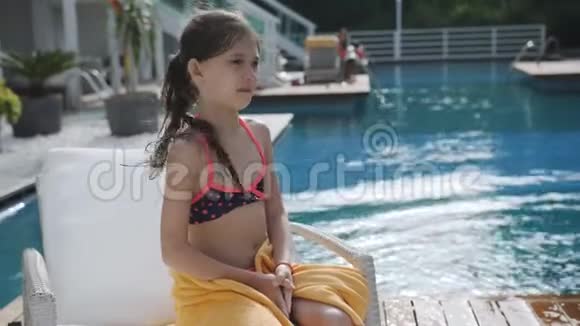 穿着泳衣坐在泳池边的小女孩裹着毛巾视频的预览图
