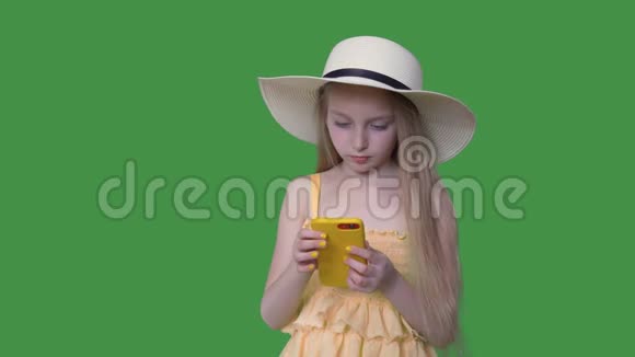 戴帽子和穿黄色衣服的年轻女孩在透明的绿色背景上使用手机有头发的夏天女孩视频的预览图