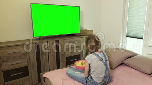 小女孩吃薯片用绿色屏幕看电视视频的预览图