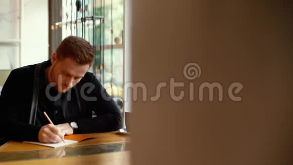 年轻人的肖像坐在咖啡馆里在记事本上作了记录视频的预览图