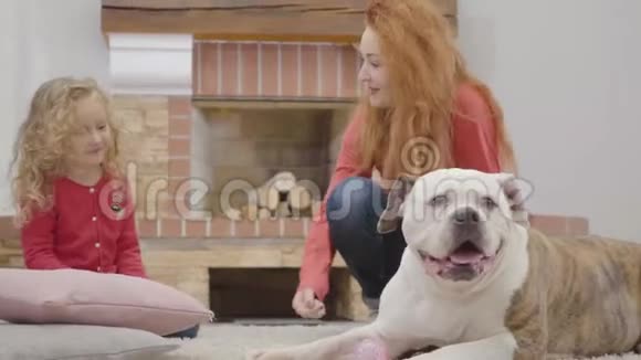 漂亮的红发白种人母亲和带着卷发和狗的女儿玩快乐的成年女人和小女孩视频的预览图