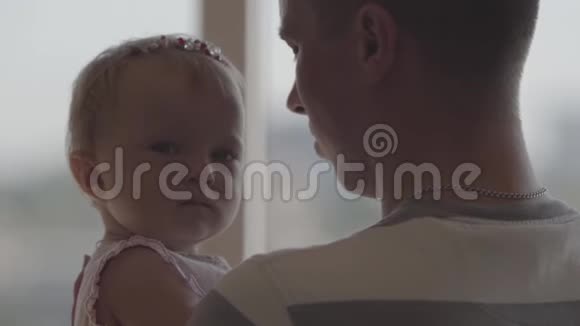 英俊的男人抱着小女孩在他的怀里在窗前特写作为父亲的乐趣可爱的家人视频的预览图