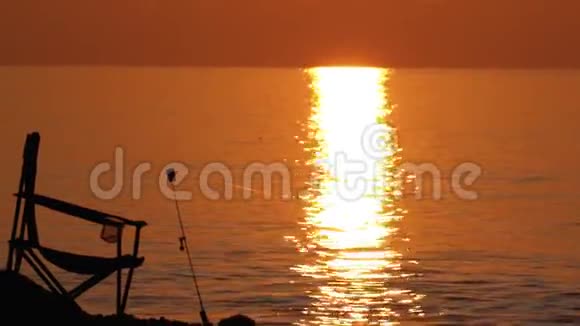 钓鱼椅和鱼竿的剪影在海边的日落小径上生活方式视频的预览图