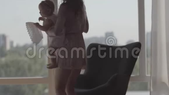 年轻漂亮的女人坐在窗前舒适的椅子上抱着女婴幸福的概念视频的预览图