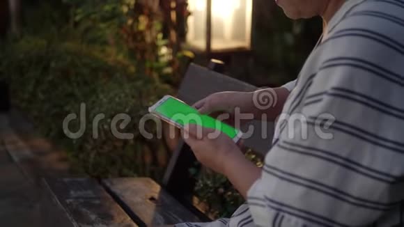 晚上在花园的智能手机里用绿色屏幕的女人手视频的预览图