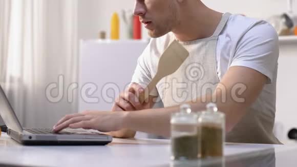 饥肠辘辘的男人在笔记本电脑上看菜谱做业余搅拌配料视频的预览图