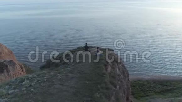 精神力量瑜伽男与女孩在莲花的位置冥想瑜伽在大自然坐在悬崖附近的海视频的预览图