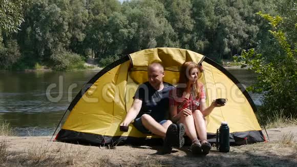 年轻的幸福夫妇来到帐篷里放松女孩吻一个男人他们有一个浪漫的时刻森林和河流视频的预览图