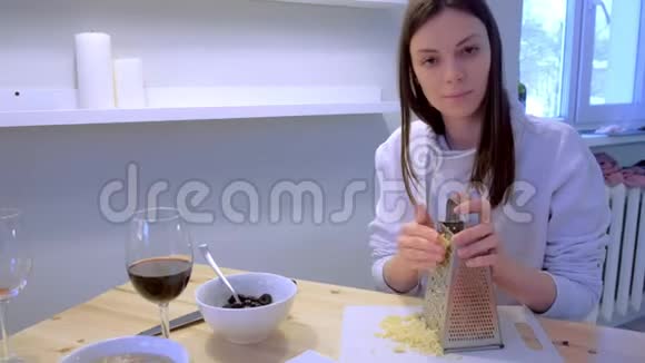 女人在家里用奶酪擦磨在厨房里喝红酒一对做晚餐视频的预览图