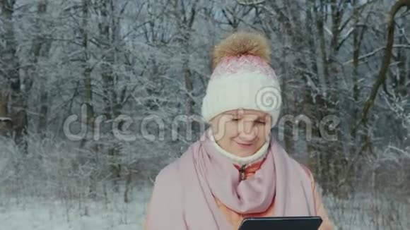 一位中年妇女在冬天的公园散步享受着一块平板电脑视频的预览图