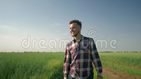 微笑的男农享受着新鲜的空气和大自然的美丽年轻人在绿茵场的背景下走向镜头视频的预览图