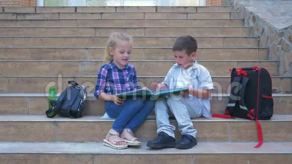 学校休息小男孩和女孩交流和复习书坐在学校台阶旁边的背包在露天视频的预览图