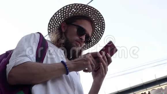 一个戴草帽和太阳镜的年轻人正在街上使用他的智能手机视频的预览图