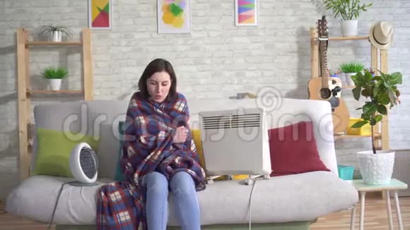 在客厅里冻僵的年轻女人在电热器旁边晒太阳视频的预览图