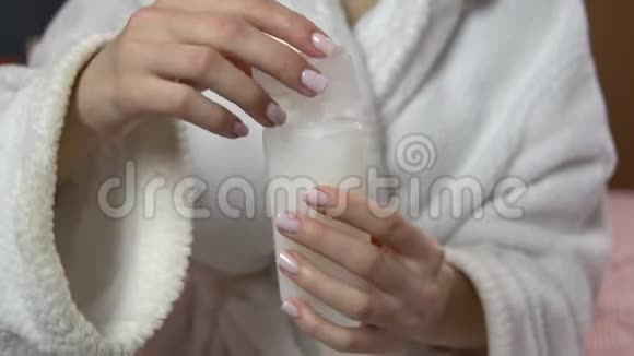 女人关上洗发水的盖子穿着浴袍的女人拿着一罐旅行洗发水特写视频的预览图