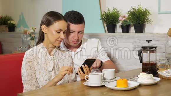 女孩和男孩在糖果店的餐桌上看手机视频的预览图