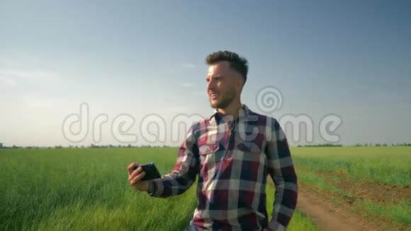 穿格子衬衫的开朗的农民手持手机在绿野蓝天的背景下自拍照片视频的预览图