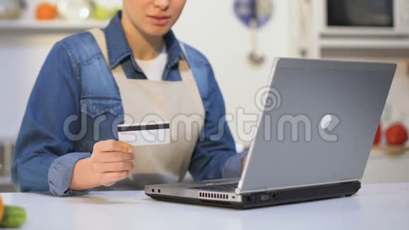 穿围裙的年轻女子在笔记本电脑上插入信用卡号码在网上购物视频的预览图
