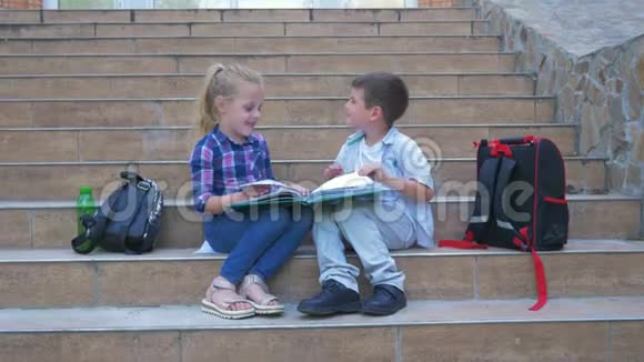 孩子们坐在学校的台阶上挨着背包在户外休息时翻阅书本视频的预览图