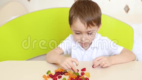 孩子坐在桌子旁手拿着吃着明亮的水果糖果果酱视频的预览图