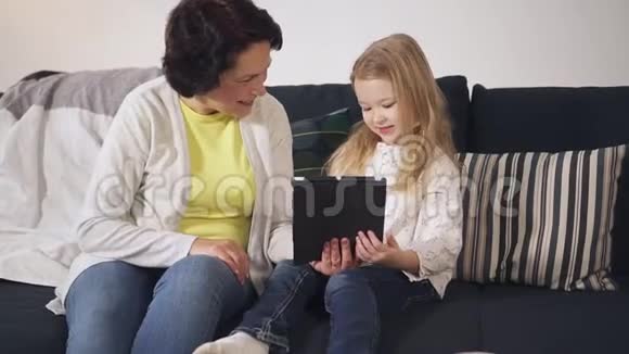笑着老奶奶和可爱的孙子正在平板电脑上看有趣的视频视频的预览图