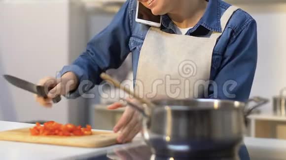 微笑的女人把切好的西红柿放进锅里做饭打电话视频的预览图