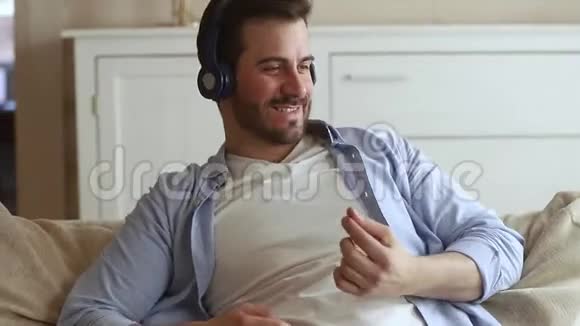 快乐的男人坐在沙发上戴着耳机听音乐视频的预览图