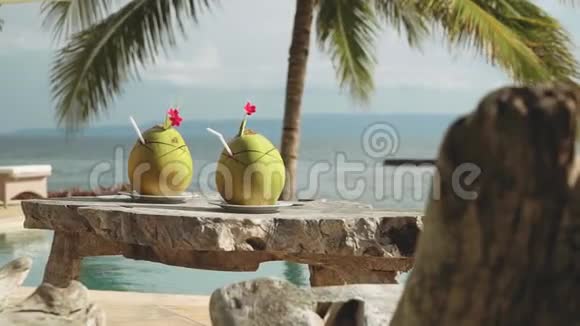 在无限游泳池和海洋前的木桌上放两杯椰子饮料视频的预览图