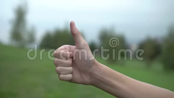 一个少年举起他的手在山坡上的一个公园里绿色的树木和天空的背景上一个OK的形状视频的预览图