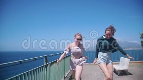 两个年轻快乐的女人在大海背景下的观景台上奔跑跳跃视频的预览图