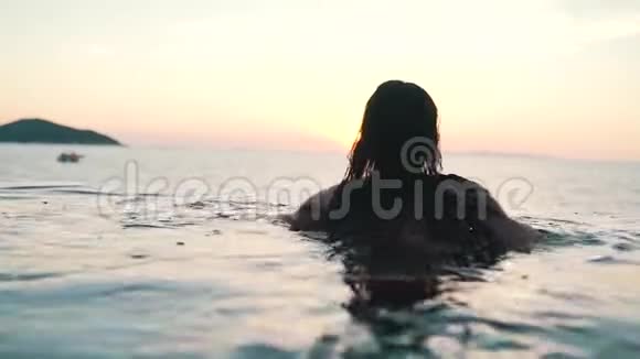 日落时分女孩在海洋背景下的泳池里瑟瑟发抖视频的预览图