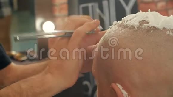 男式沙龙中带直剃刀的秃头剃光头把剃须刀贴在理发店的光头视频的预览图