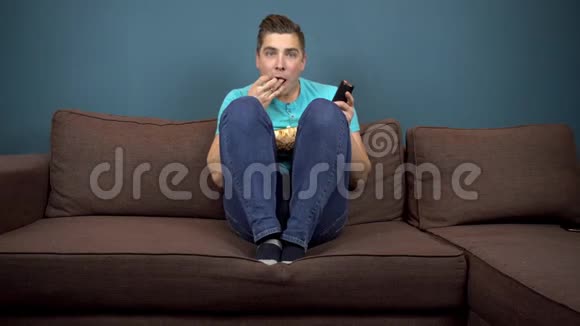 一个年轻人正在看电视和吃爆米花那家伙正在仔细看电视一个激动人心的时刻视频的预览图