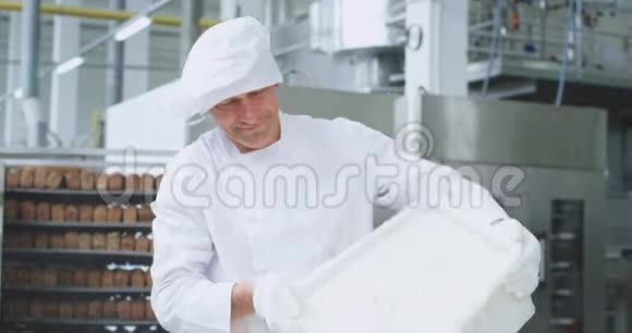 老面包师准备面团时他把面粉放入一个工业容器的特写中他直视着视频的预览图
