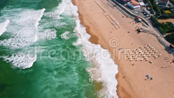 与游客一起度假在沙滩上观看海浪的顶部鸟瞰图翡翠绿色海洋表面葡萄牙辛特拉视频的预览图