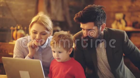 可爱的小男孩看着笔记本电脑屏幕和父母在家看动画片快乐的爸爸妈妈和小男孩视频的预览图