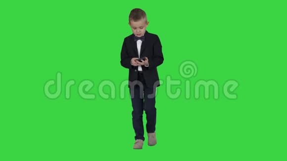 穿着服装走路和使用智能手机的小男孩在绿色屏幕上Chroma键视频的预览图