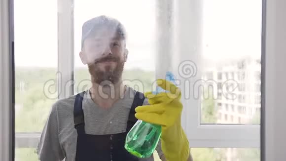 漂亮的男洗手装蓝色工作服在窗户上喷洒清洁剂并用一种特殊的视频的预览图